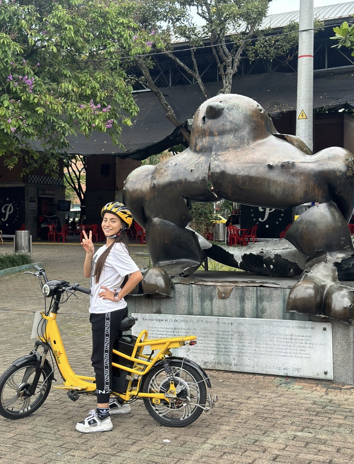 Niña con casco en tour de bicicleta eléctrica junto al Pájaro de Paz de Botero, Plaza San Antonio, Medellín
