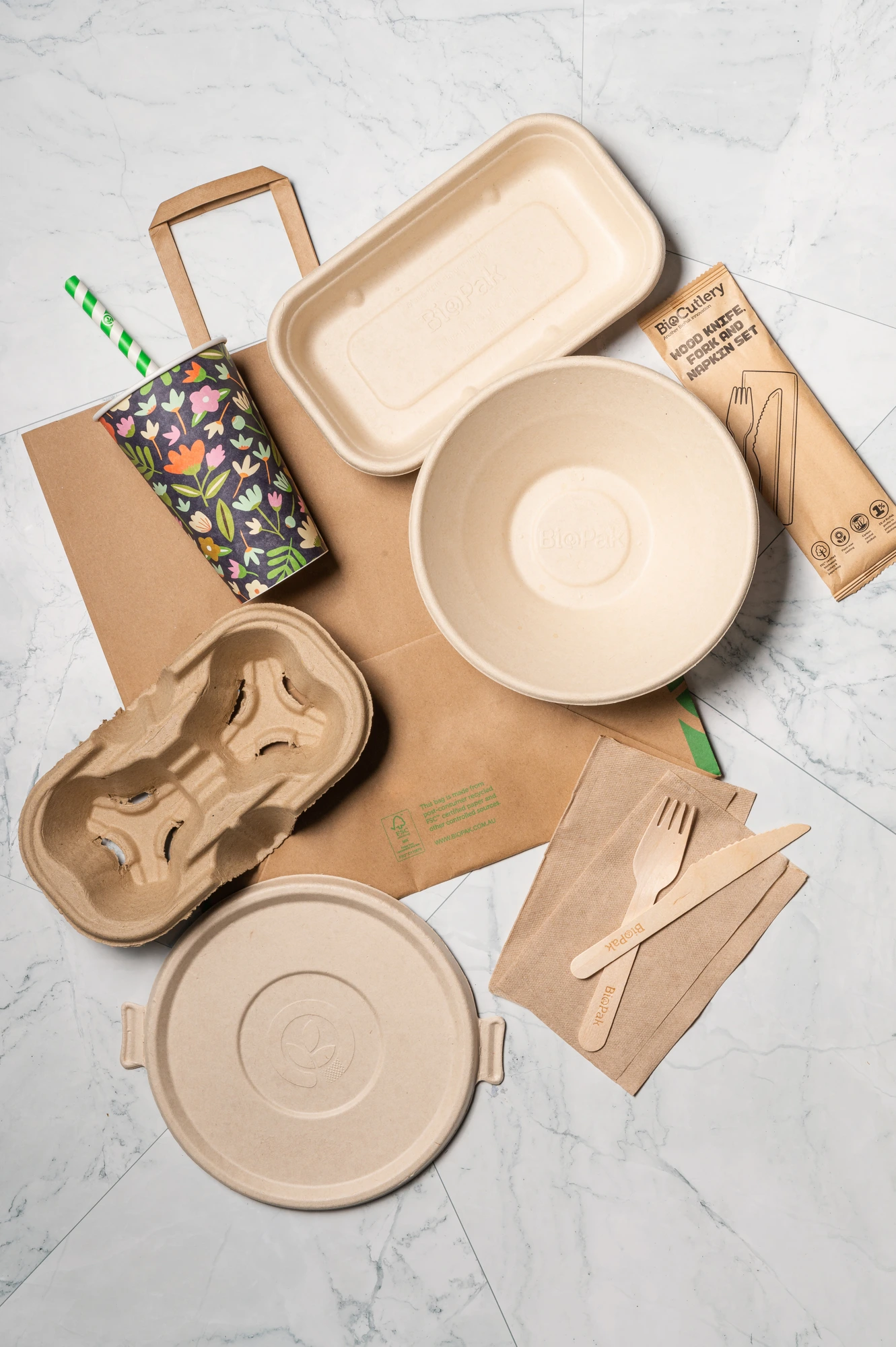 Top-down view of BioPak compostable packaging products including cups, containers and cutlery arranged neatly
