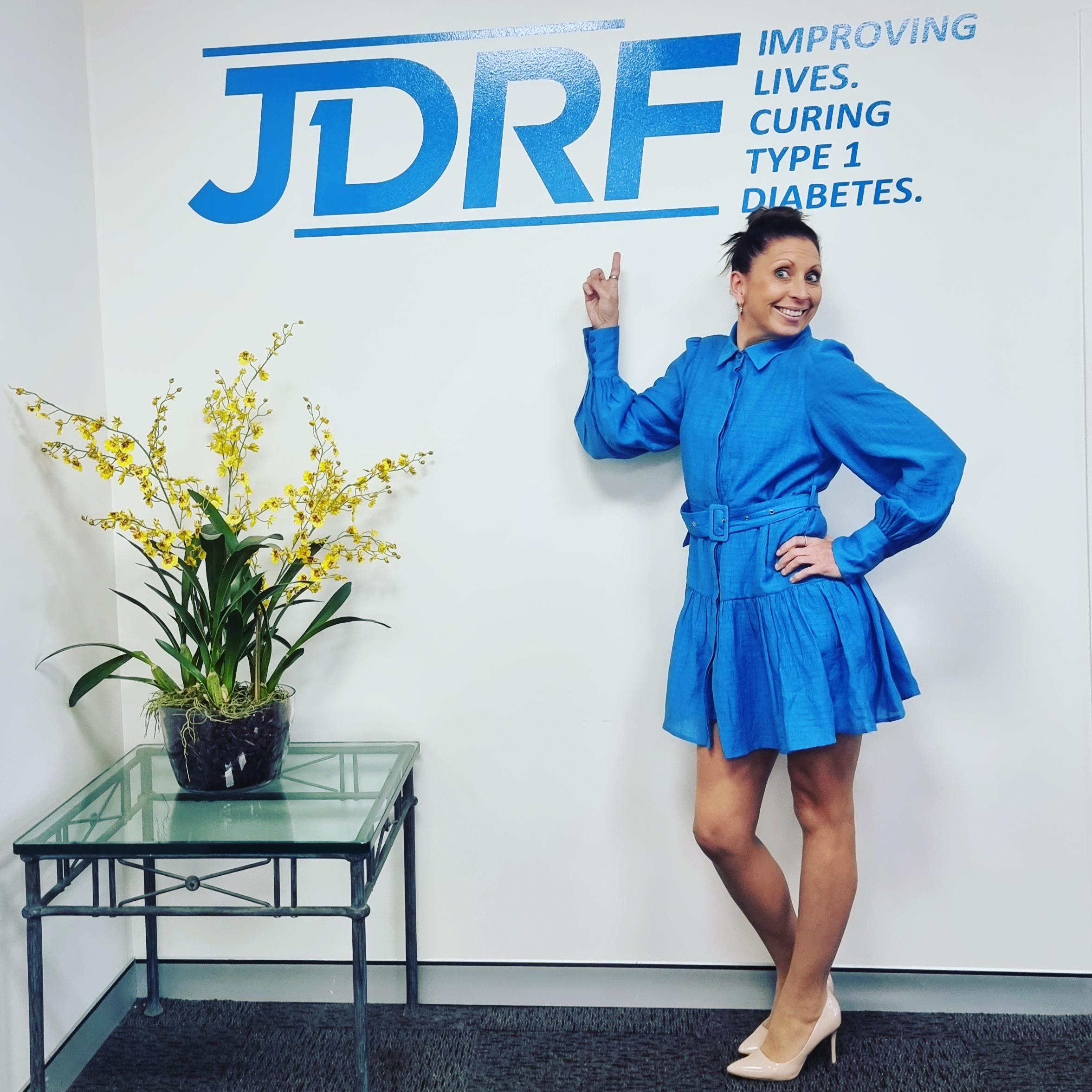 Louise in a blue dress pointing at the JDRF / BreakthroughT1D backdrop