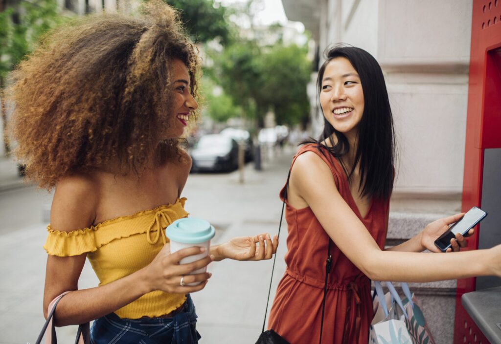 Two friends using ATM machine on city street