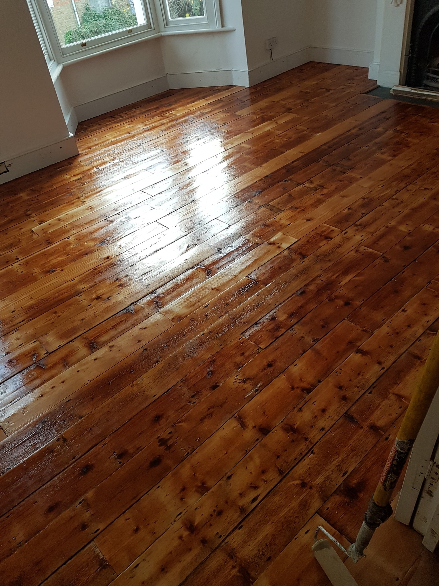 Freshly sanded and varnished pine floorboards in a bright bay-windowed room