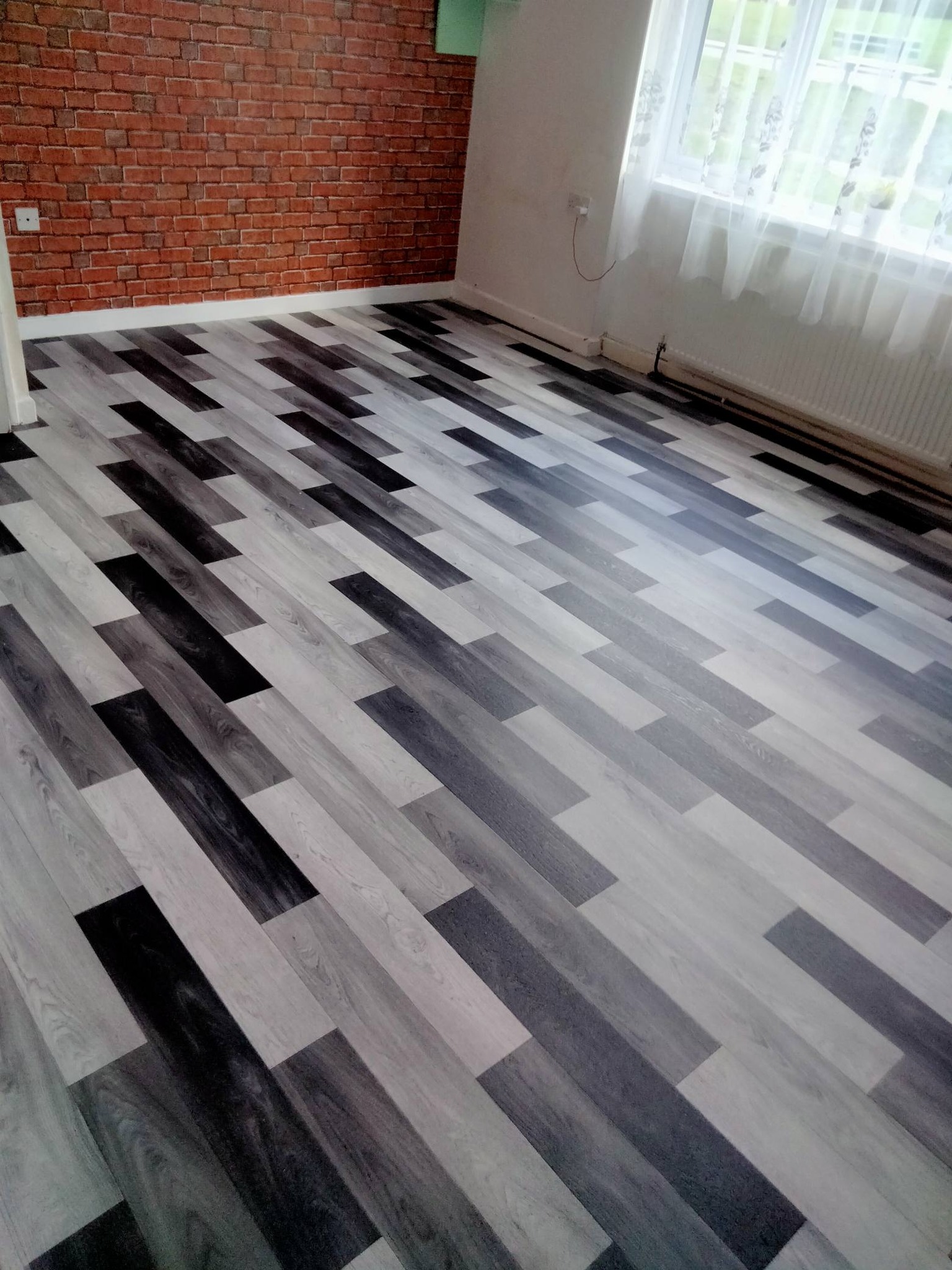 Bold grey and charcoal mixed-tone laminate flooring in a room with exposed brick wall