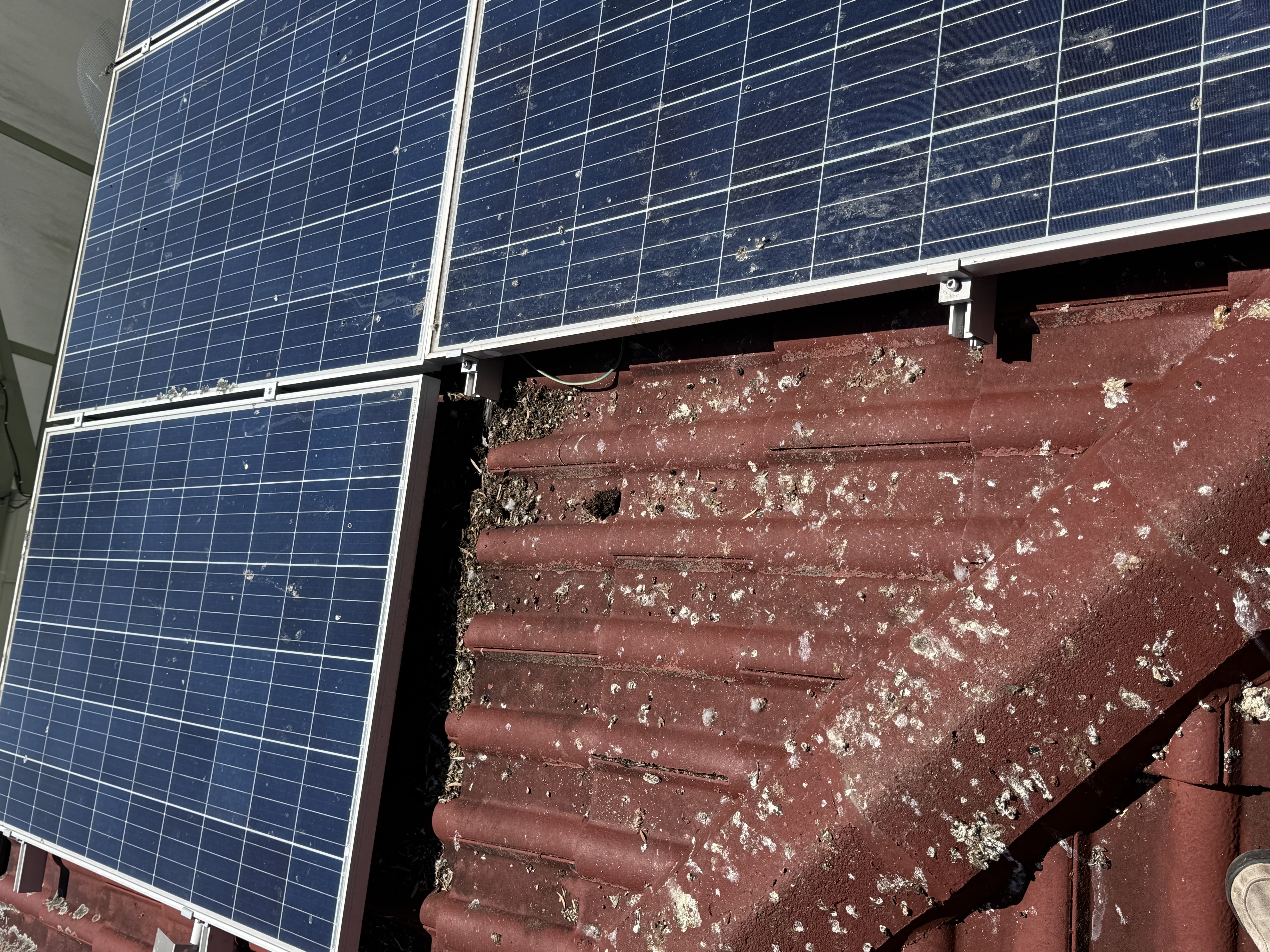 Dirty tile roof under solar panels with debris