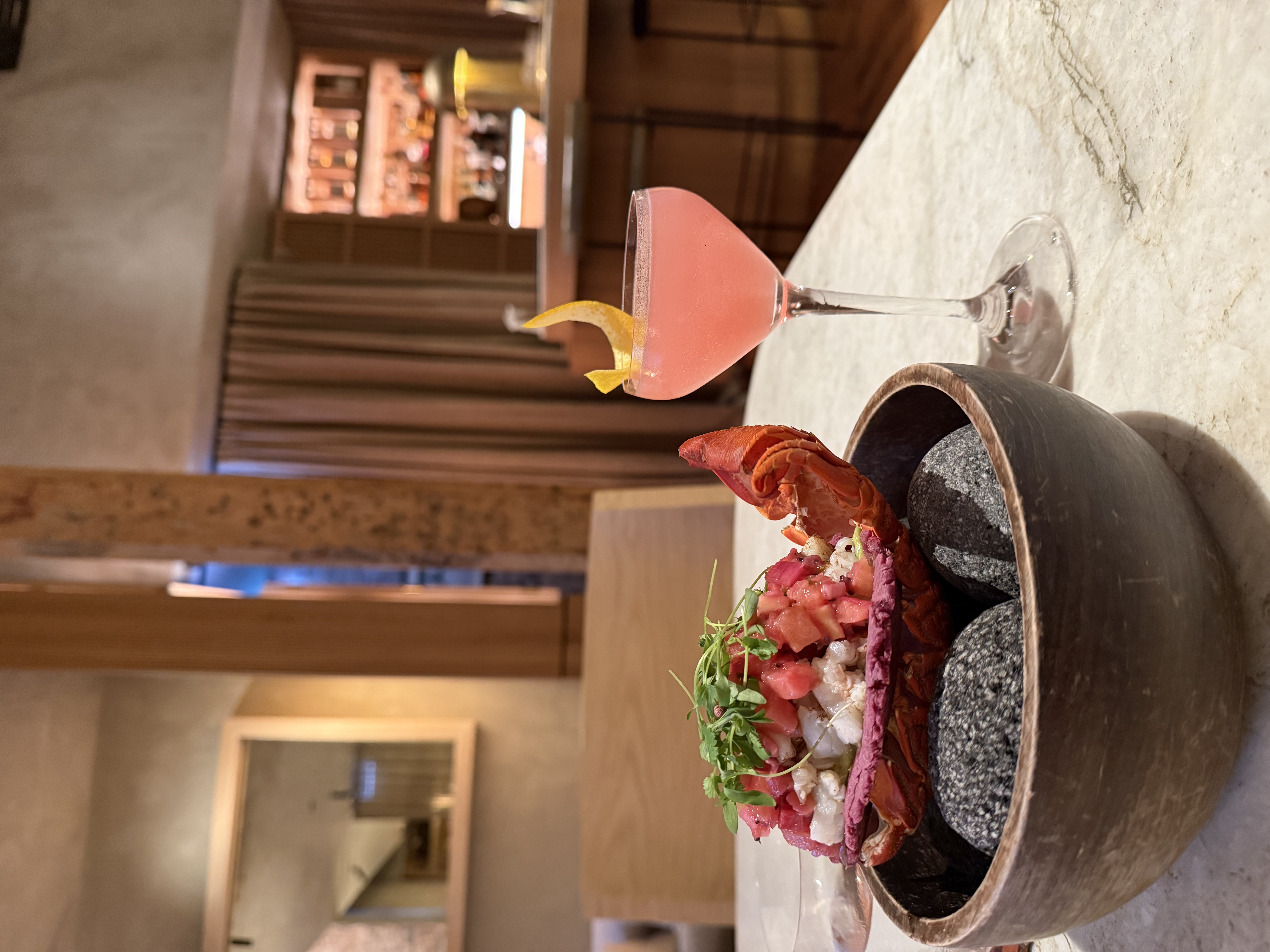 Lobster crudo and a coral-pink cocktail on a marble bar