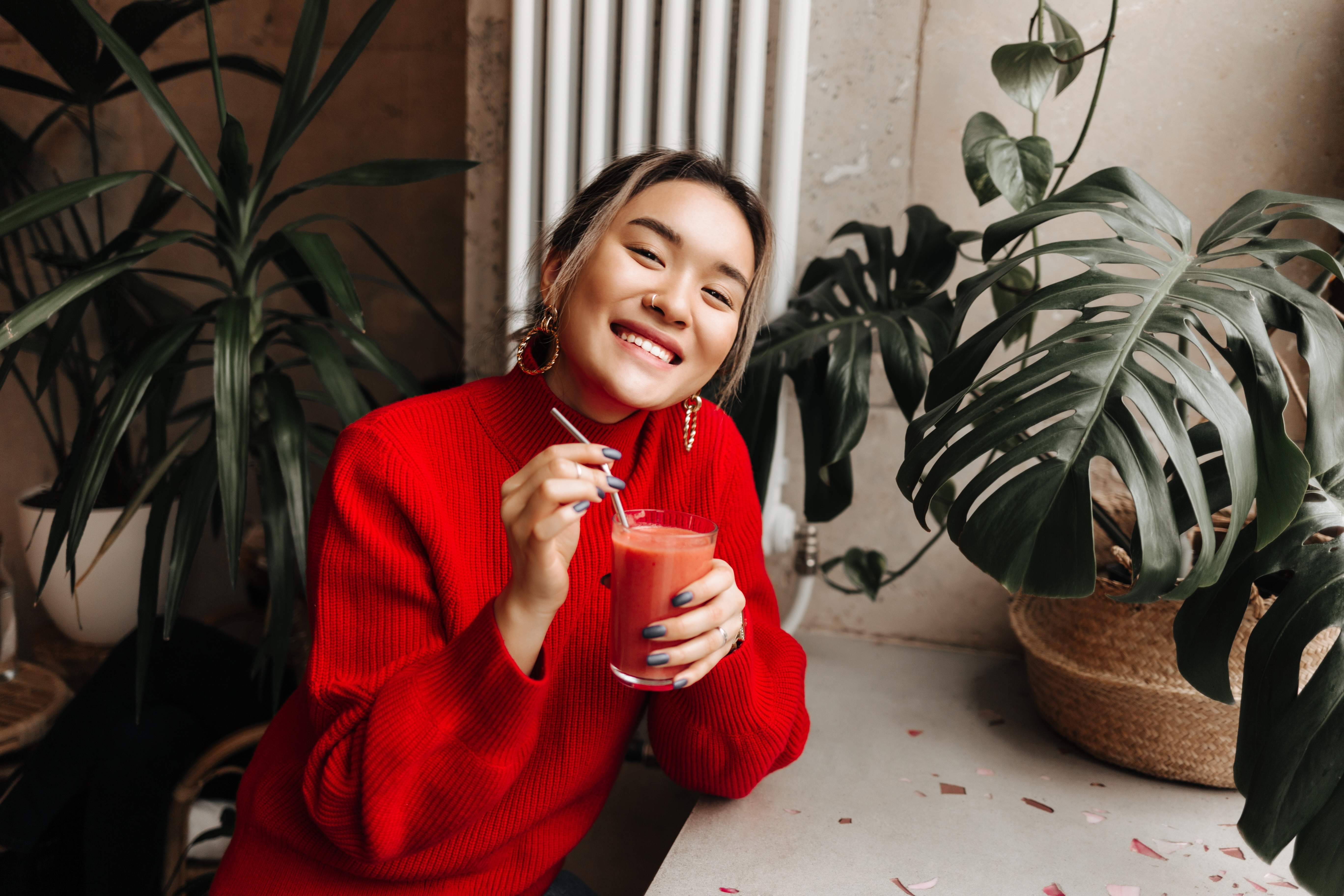 A woman in a red sweater smiling warmly with a drink, surrounded by plants — storytelling that connects