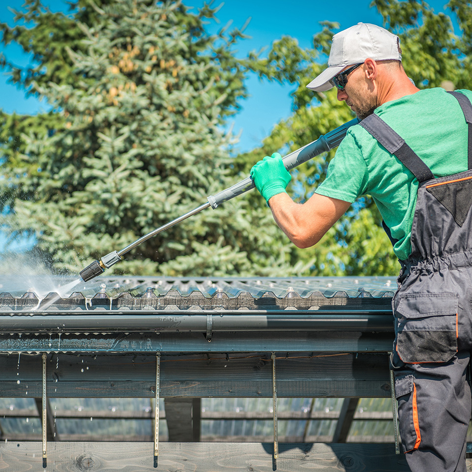 A New Zealand tradie maintaining a home — pressure-washing the roof and gutters