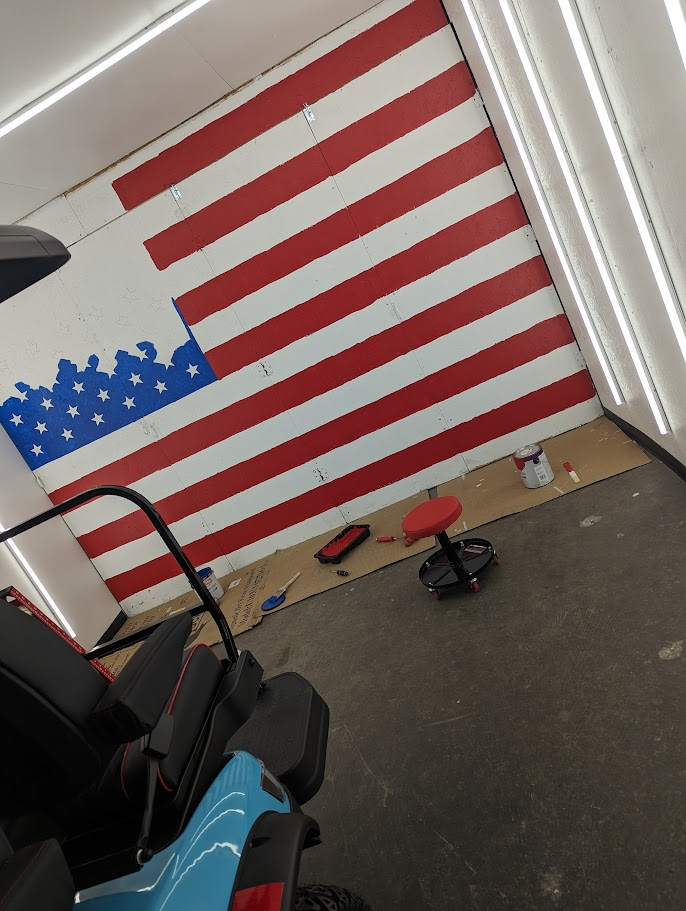 The first hand-painted American flag mural on the wall of Jake's Custom Carts original Tampa shop in 2024, with a teal custom cart parked in front — a signature touch the shop has carried into every subsequent location