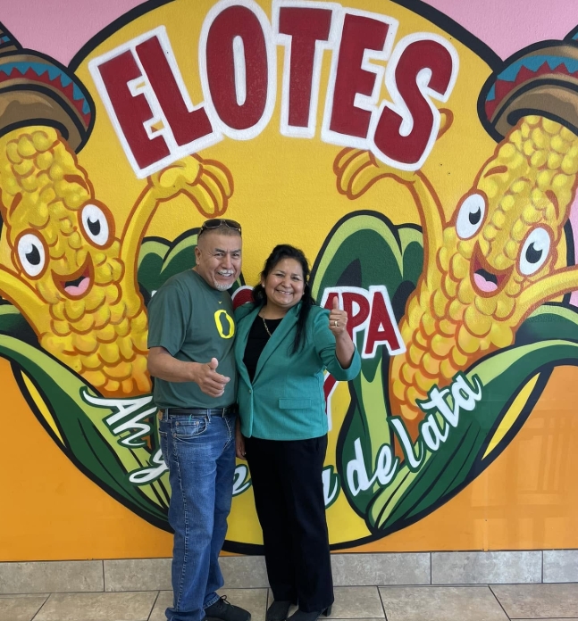 The owners of Elotes El Compa Chuy in front of their mural