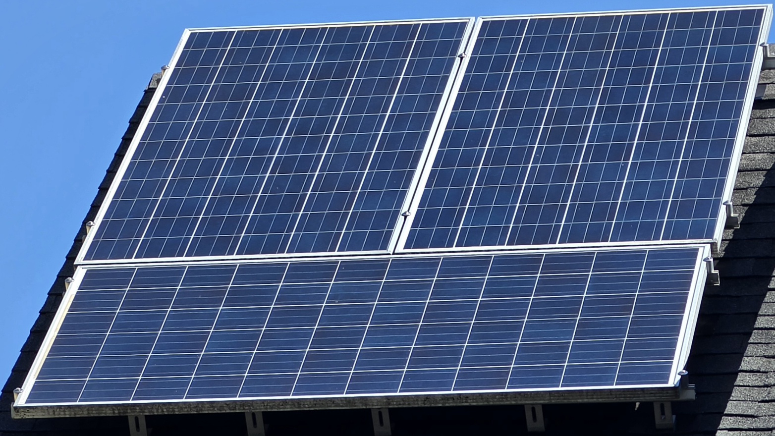 Close-up of two rows of solar panels on a shingle roof — the top row shows uniform deep-black factory finish after cleaning, while the bottom row remains visibly lighter and mottled due to EVA encapsulant yellowing that no surface cleaning can restore