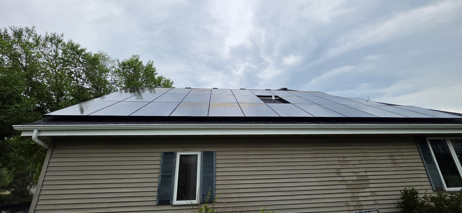 Solar panel array on a tan-siding home BEFORE cleaning — panels look uniformly dark because accumulated dust is masking any underlying discoloration