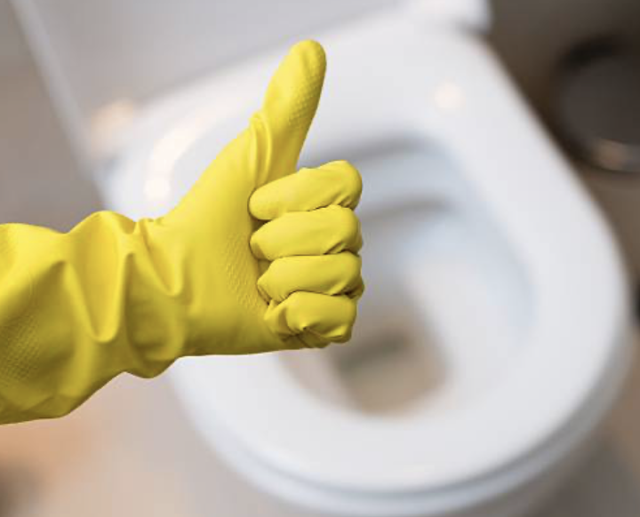 Cleaning technician in yellow rubber glove giving a thumbs-up next to a freshly sanitized white toilet