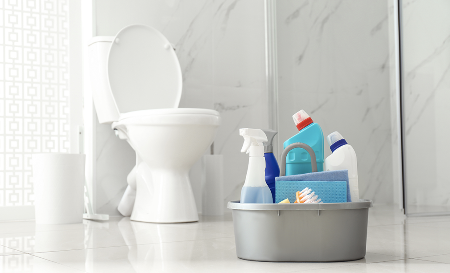 Modern marble bathroom with a clean white toilet and a caddy of cleaning supplies on the floor