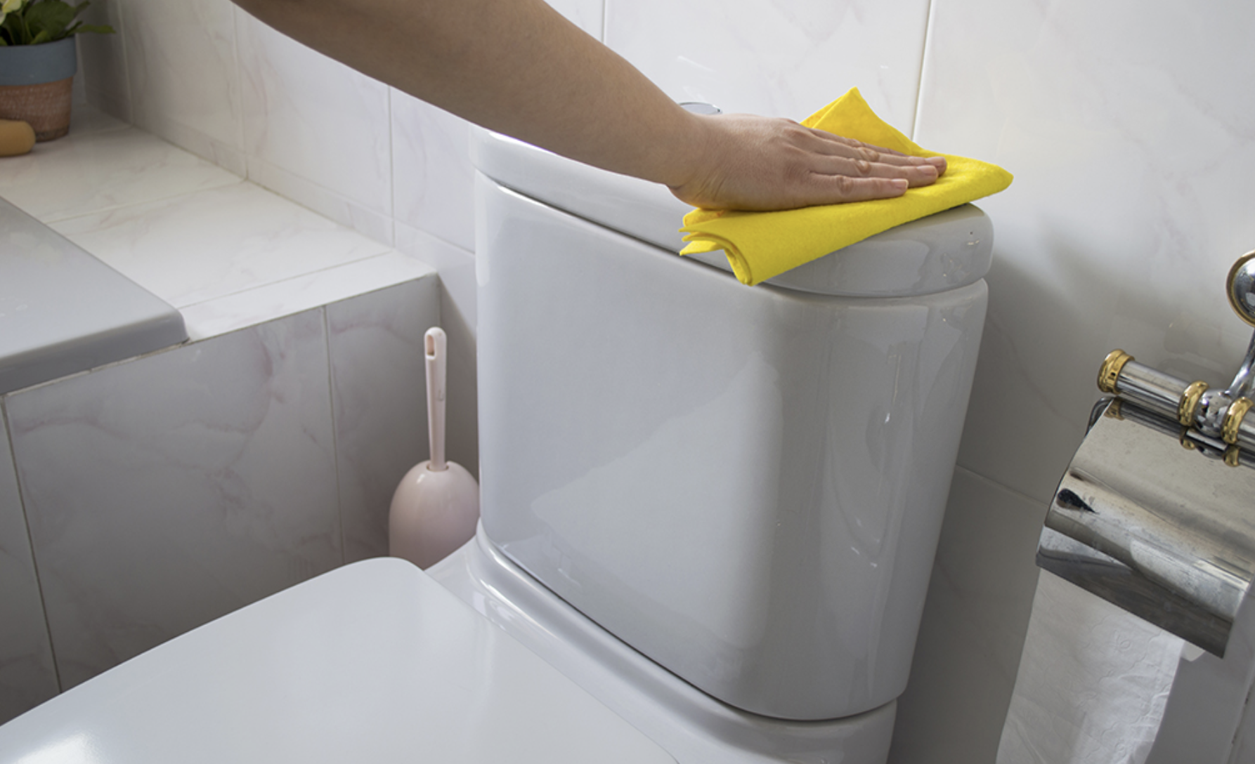 Cleaning technician in yellow rubber gloves wiping a toilet seat with a sponge