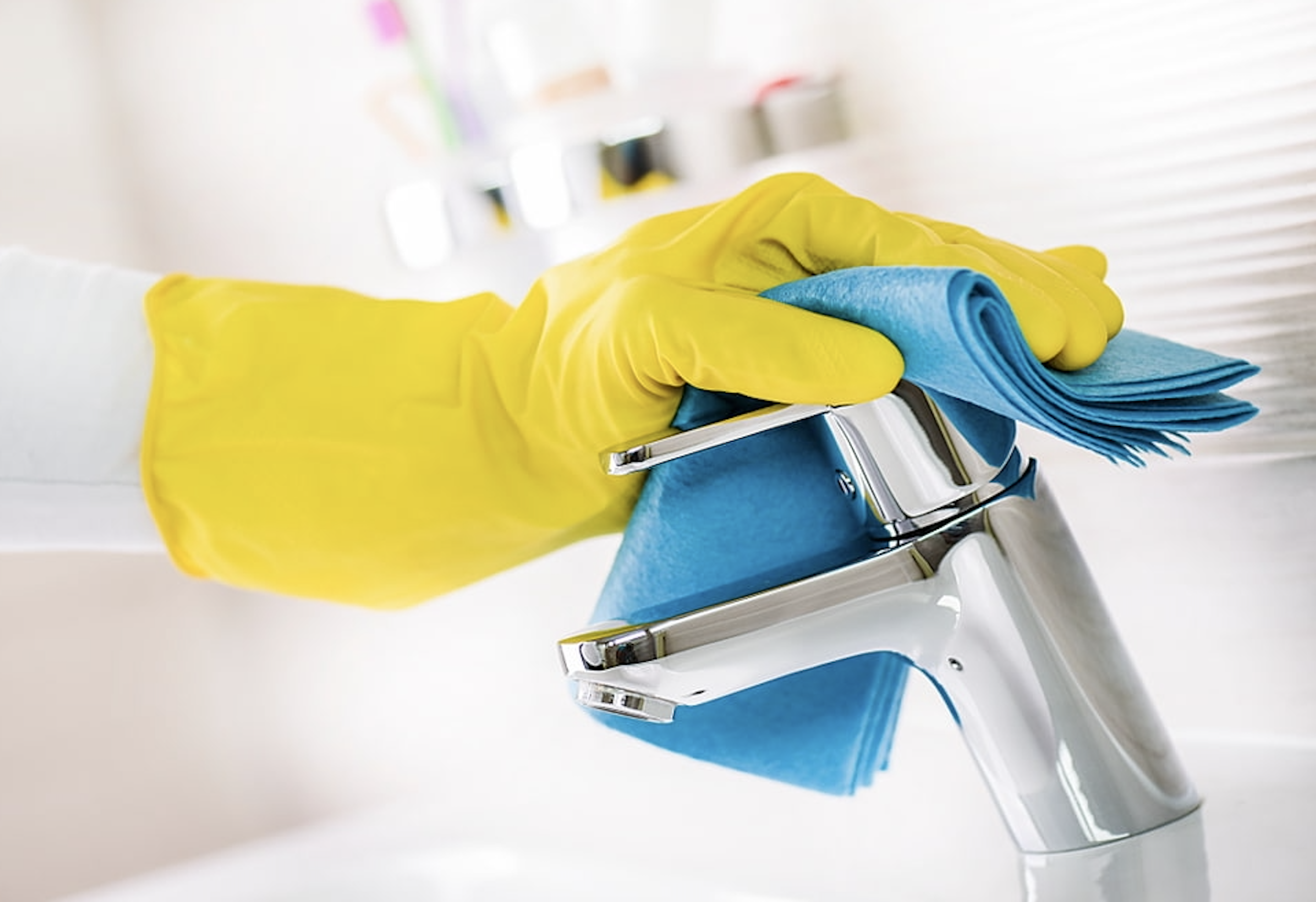 Cleaning technician in yellow rubber glove wiping a chrome restroom faucet