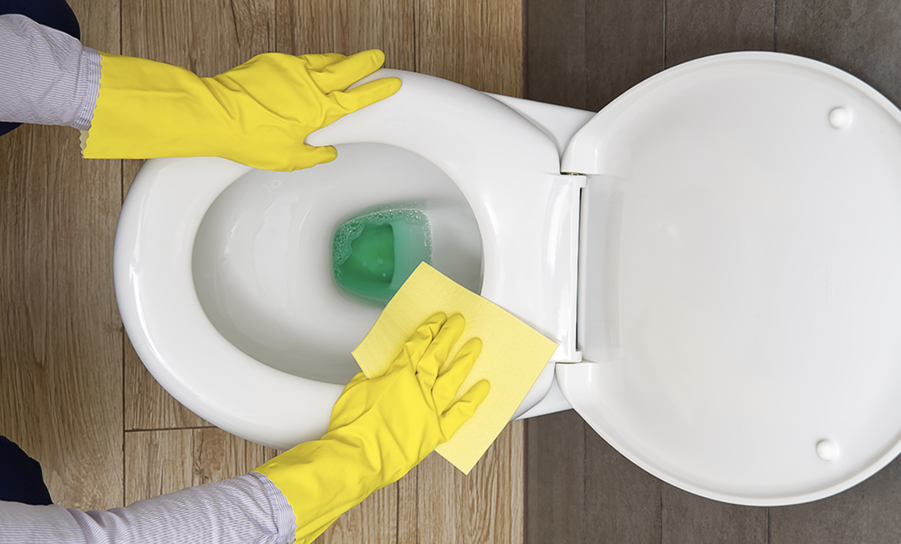 Hand wiping the tank of a white toilet with a microfiber cloth in a clean marble restroom