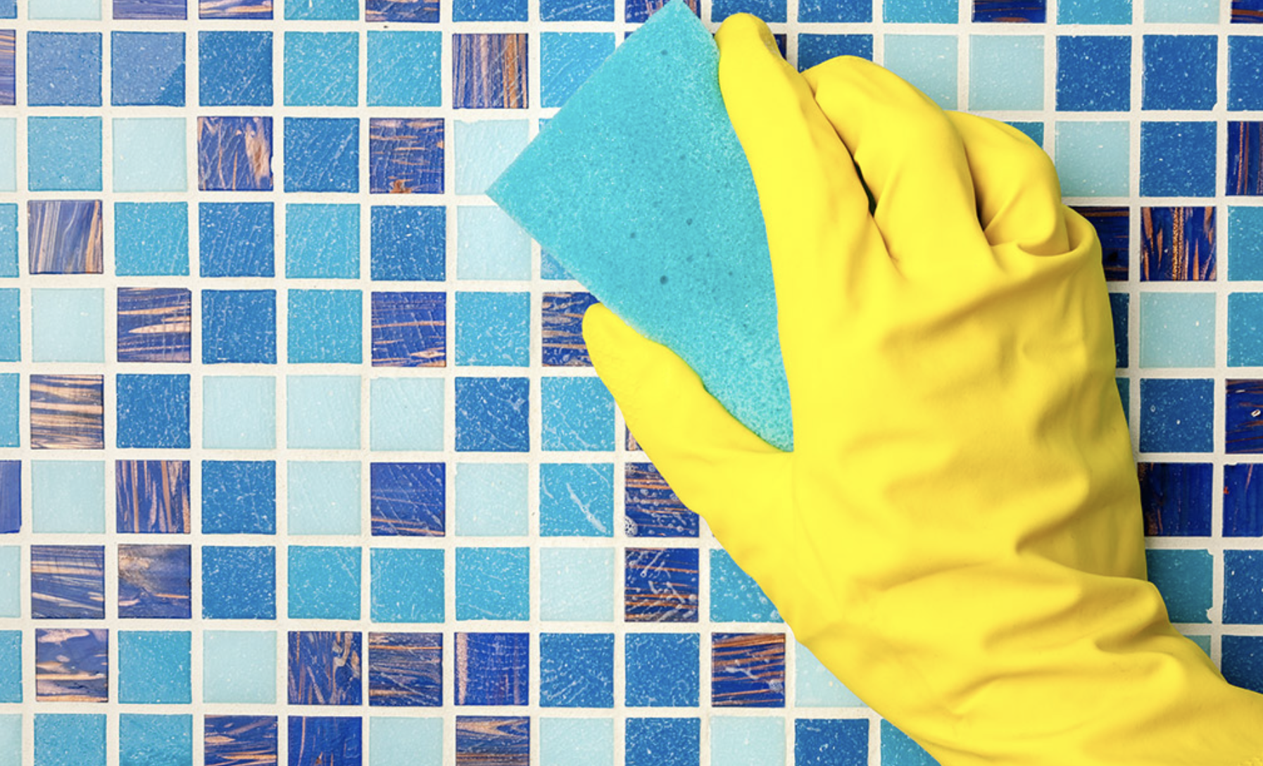 Yellow-gloved hand using a sponge to scrub blue mosaic tile and grout