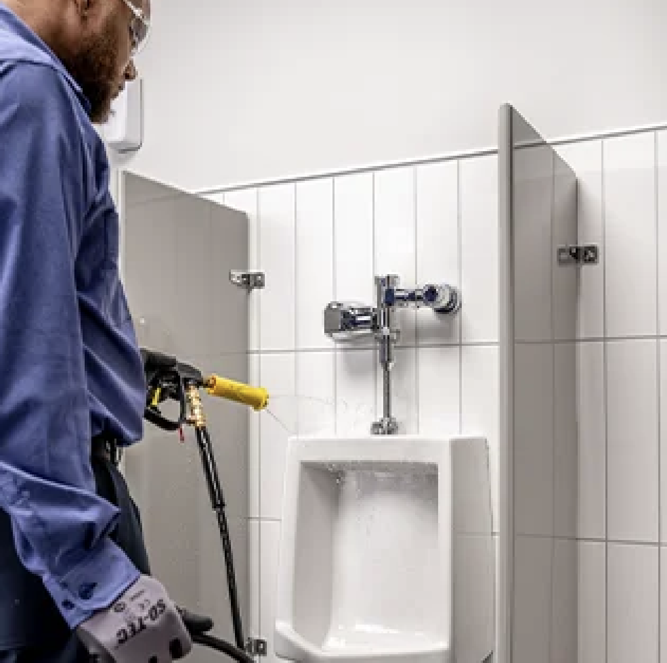Commercial cleaning technician using a deep-foam pressure gun to sanitize a urinal in a commercial restroom