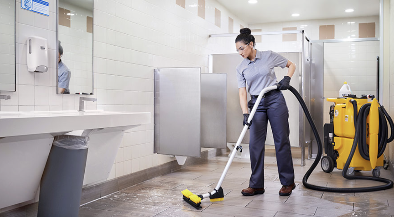 Cleaning technician using a powered floor scrubber on the tile floor of a commercial restroom