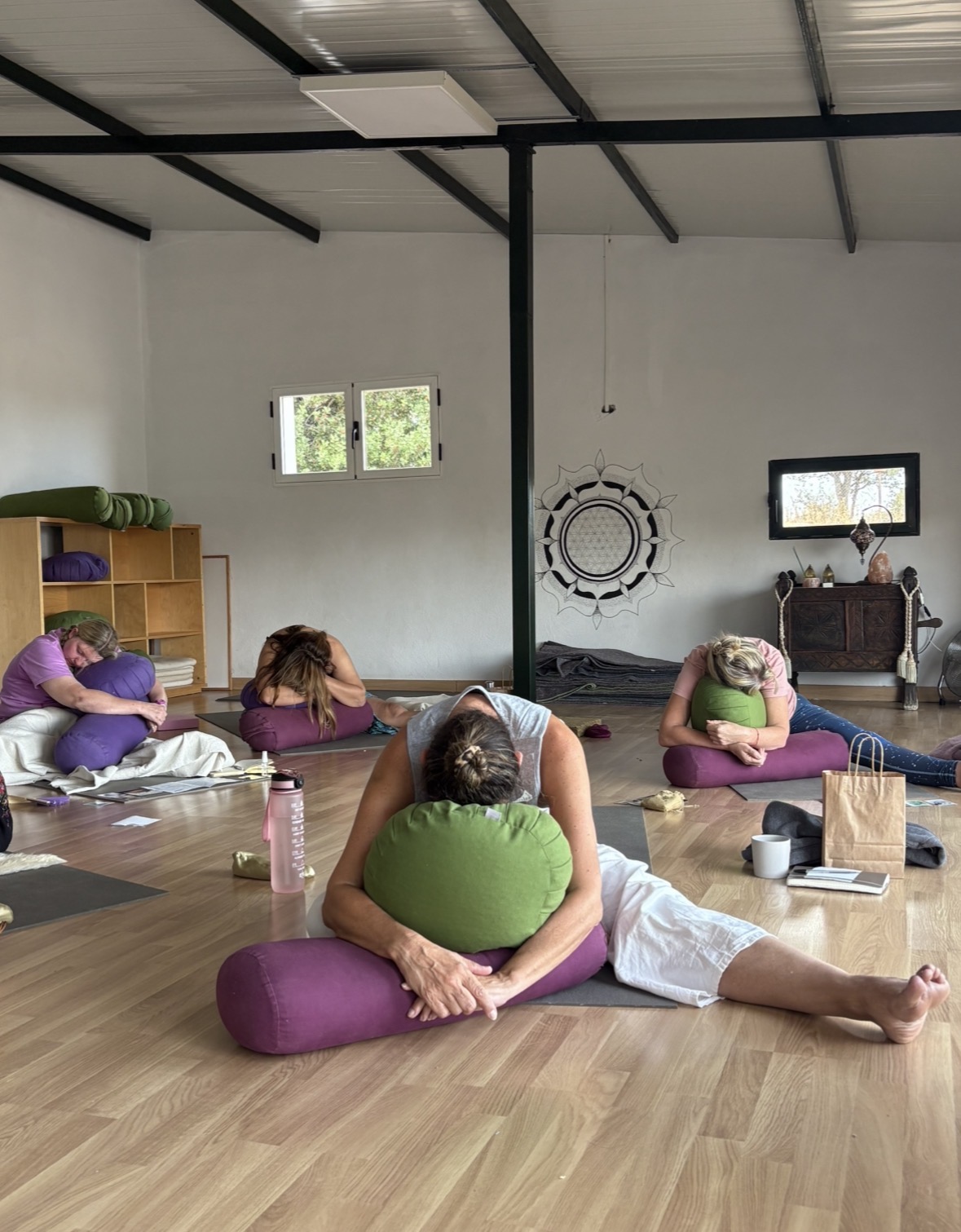 Yin yoga class with students in supported forward fold using bolsters, practicing deep release in a peaceful studio