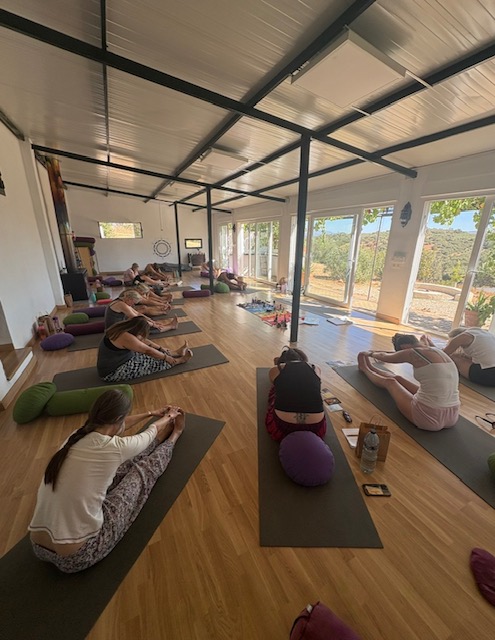 Yoga retreat participants practicing forward fold with bolsters in Spanish studio