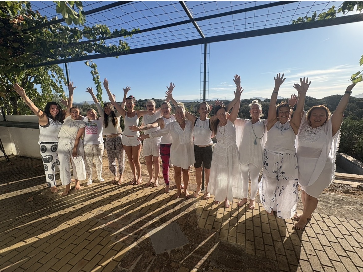 Joyful yoga retreat group with arms raised on rooftop terrace in Spain with mountain views
