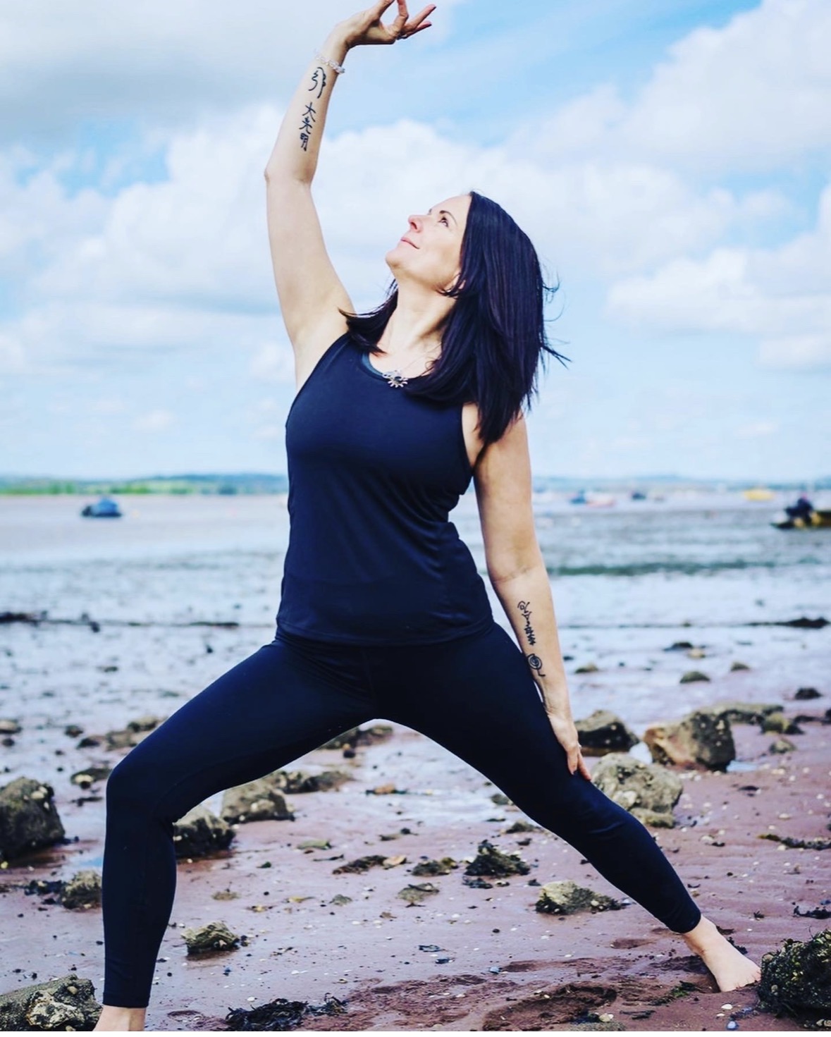 Annelie Lily demonstrating reverse warrior pose (Viparita Virabhadrasana) on a beach at low tide