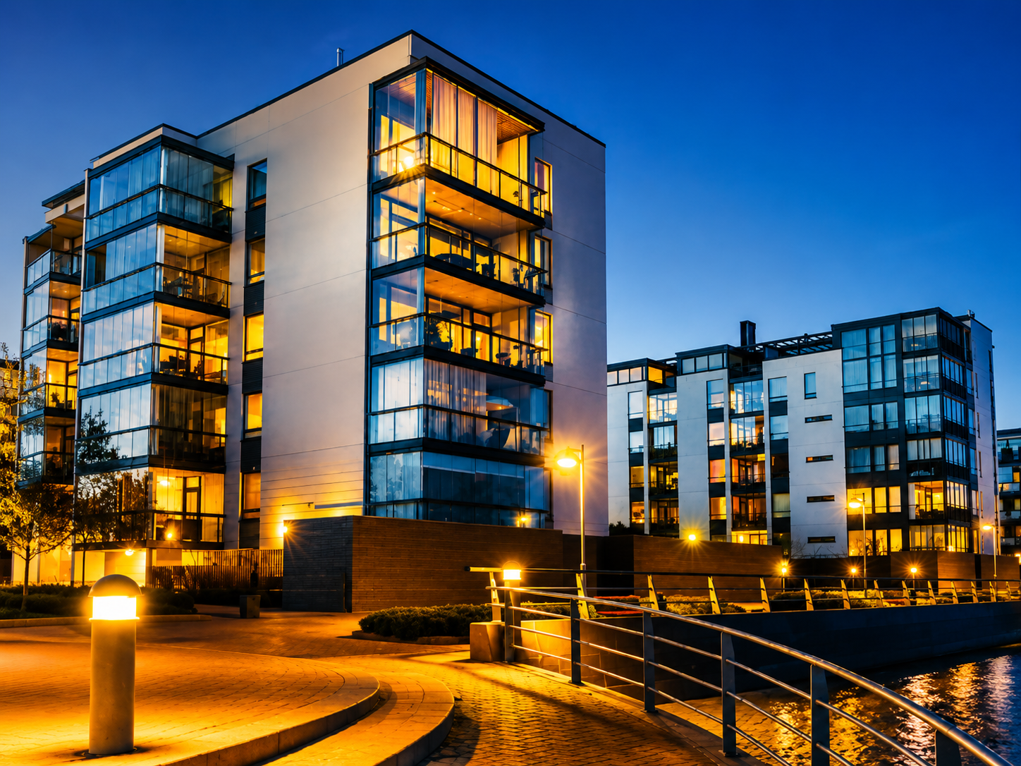 Modern glass-fronted apartment building serviced by Noble Empire — illuminated balconies along a lit waterfront promenade