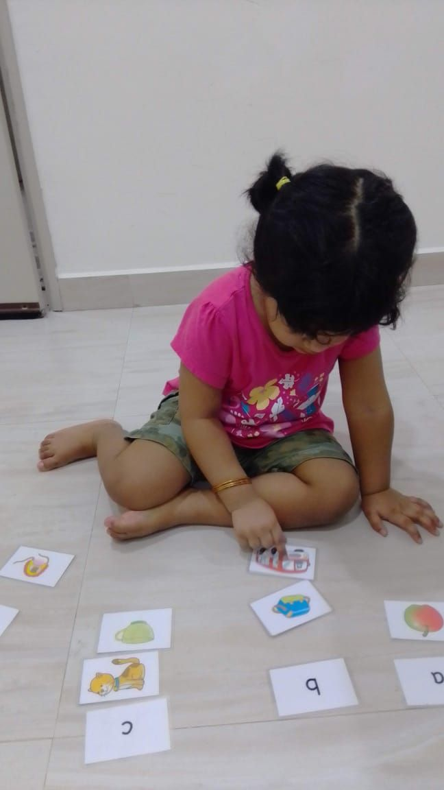 A young child kneeling on the floor matching letter and picture cards.