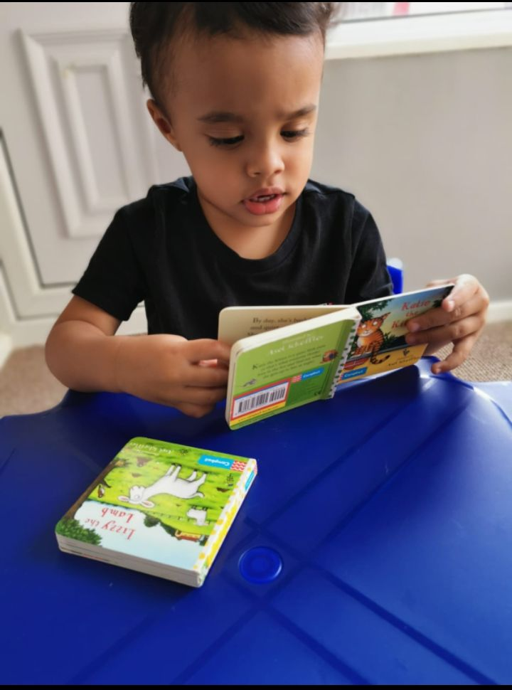 A young boy concentrating quietly while exploring a board book at his table.