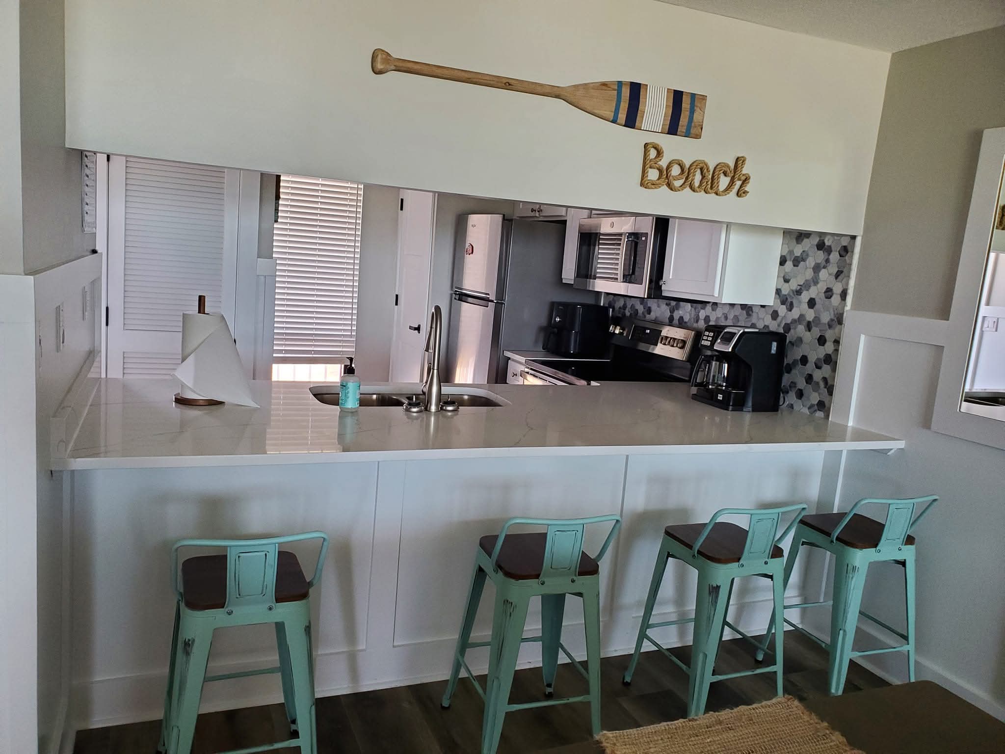 Spotless beach-themed kitchen with mint bar stools and stainless appliances