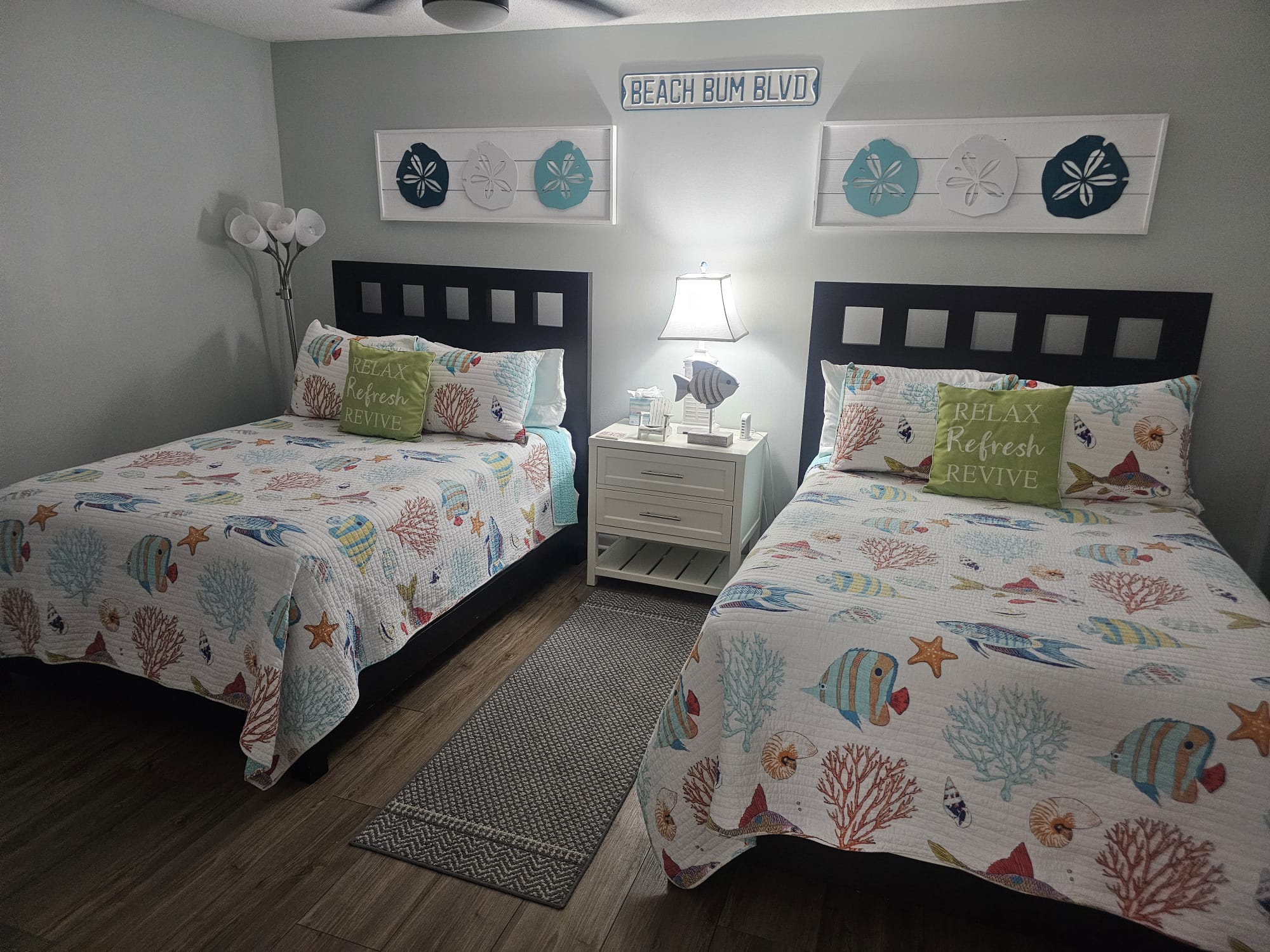 Twin beds bedroom freshly made with coastal fish quilts and Beach Bum Blvd sign