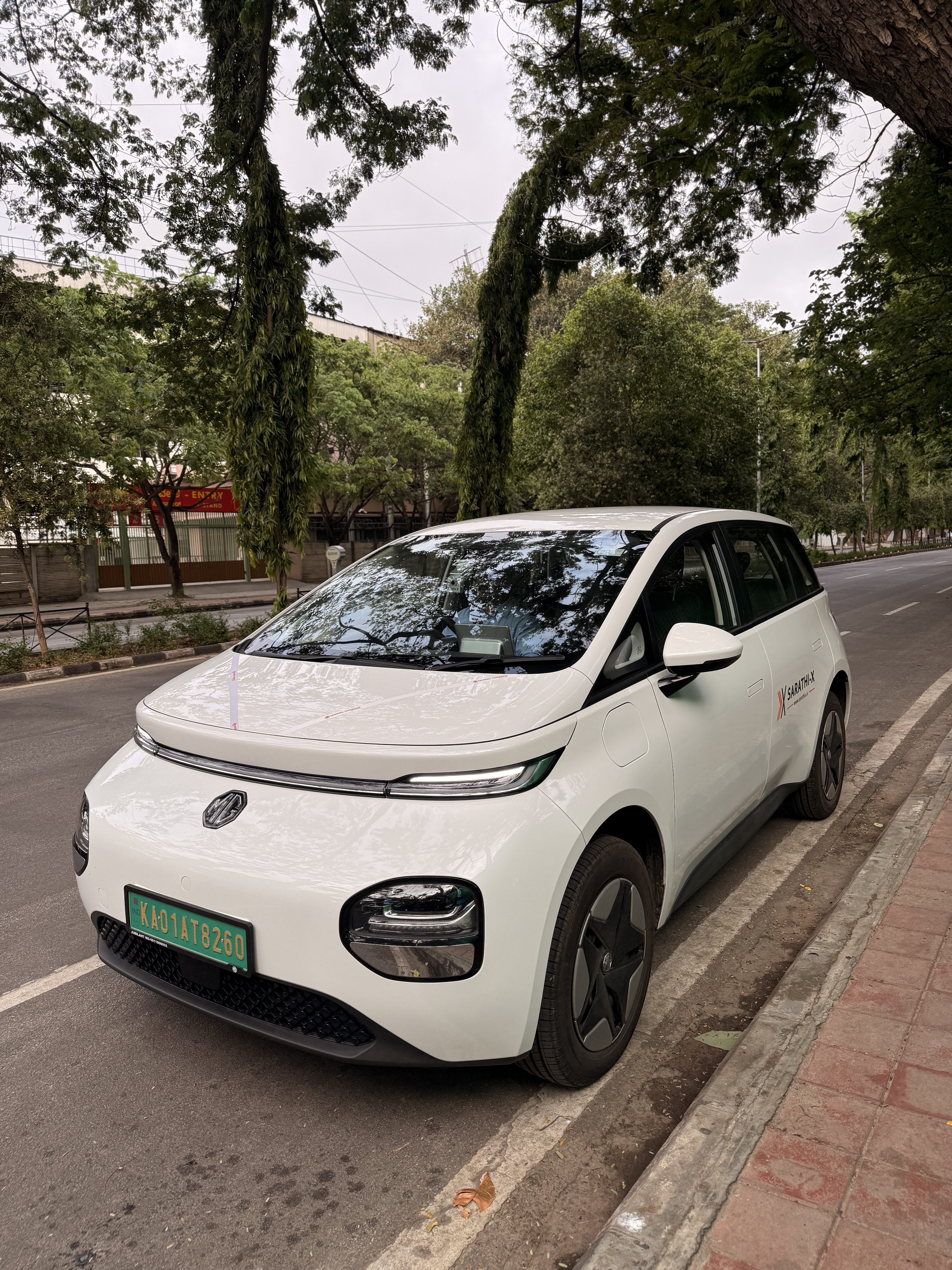 Sarathi-X MG Windsor EV (KA01AT8260) parked on a tree-lined Bengaluru street