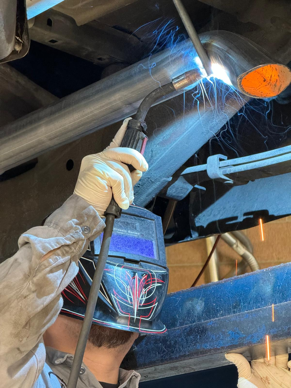 Welder working under car welding exhaust pipes
