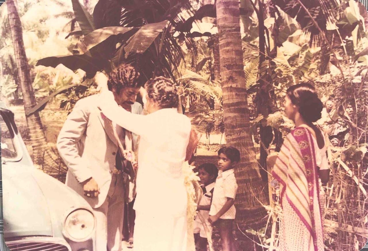 A wedding day in Potta — a white Ambassador, coconut palms, and family gathered under the trees.
