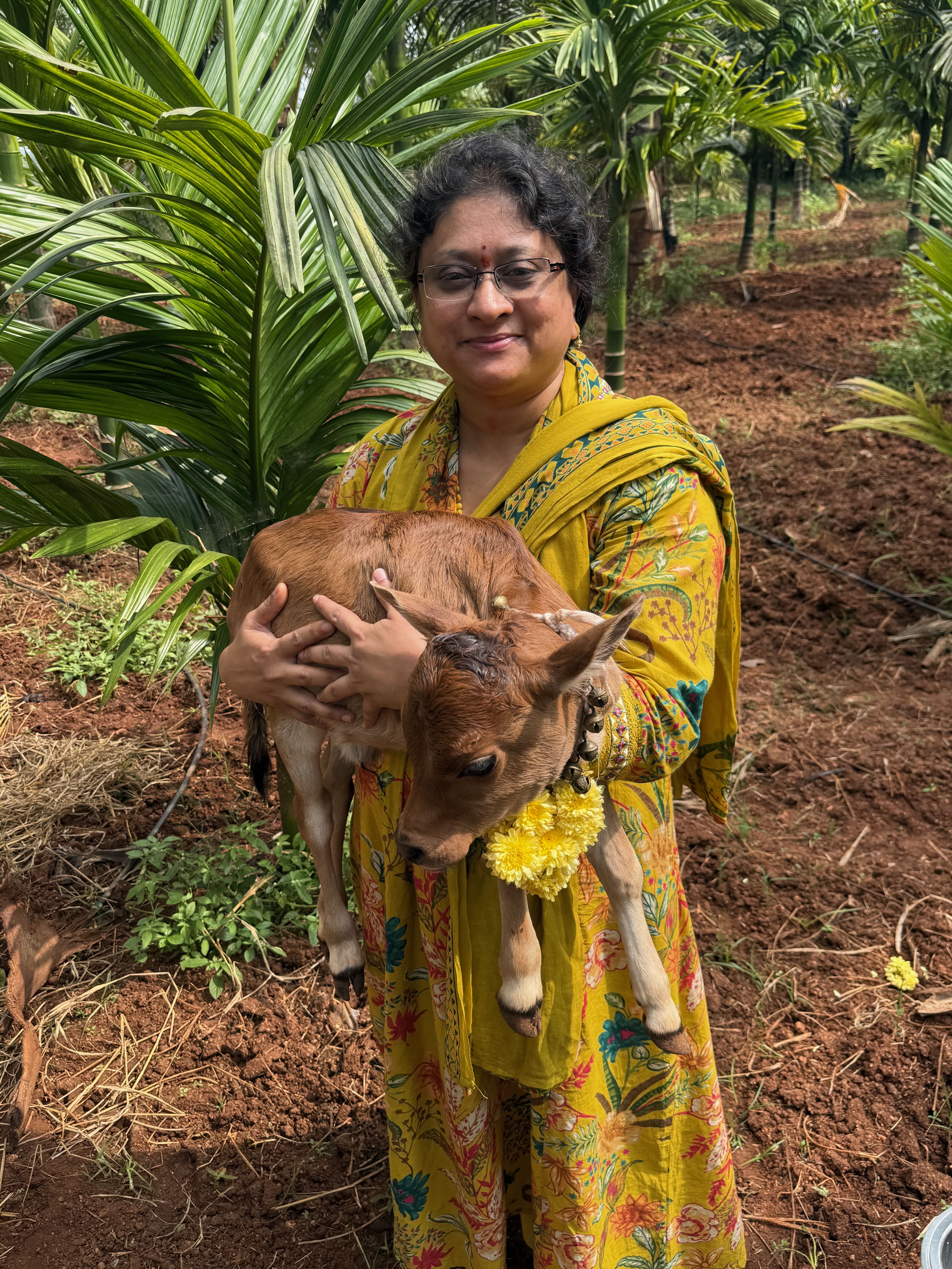 Nandini Vishwanathapura holding a calf with marigold garland at Bilva Farms