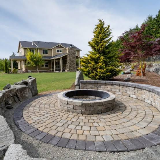 M&L Exterior Design — Circular paver patio with custom stone fire pit and seating wall