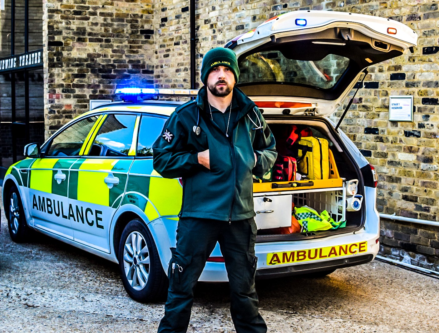 Kirk standing at the back of ambulance with blue lights on