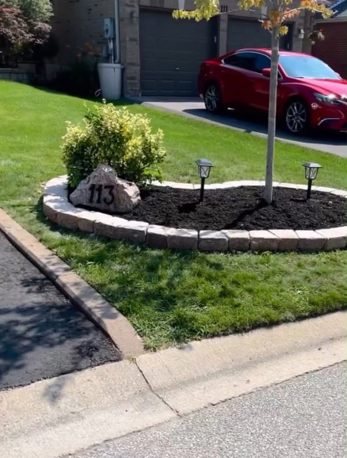 Curbed mulch bed with natural stone border, shrubs, custom house-number boulder and solar path lights