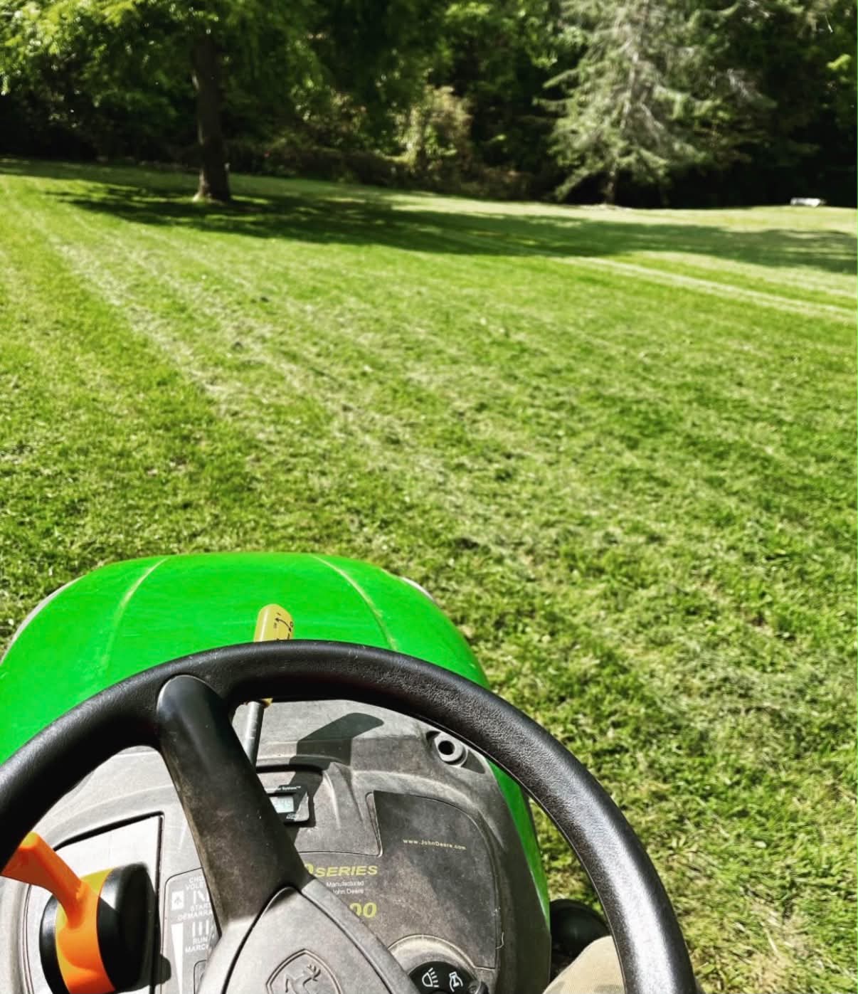 Driver's-eye view of a John Deere riding mower cutting a wide green lawn