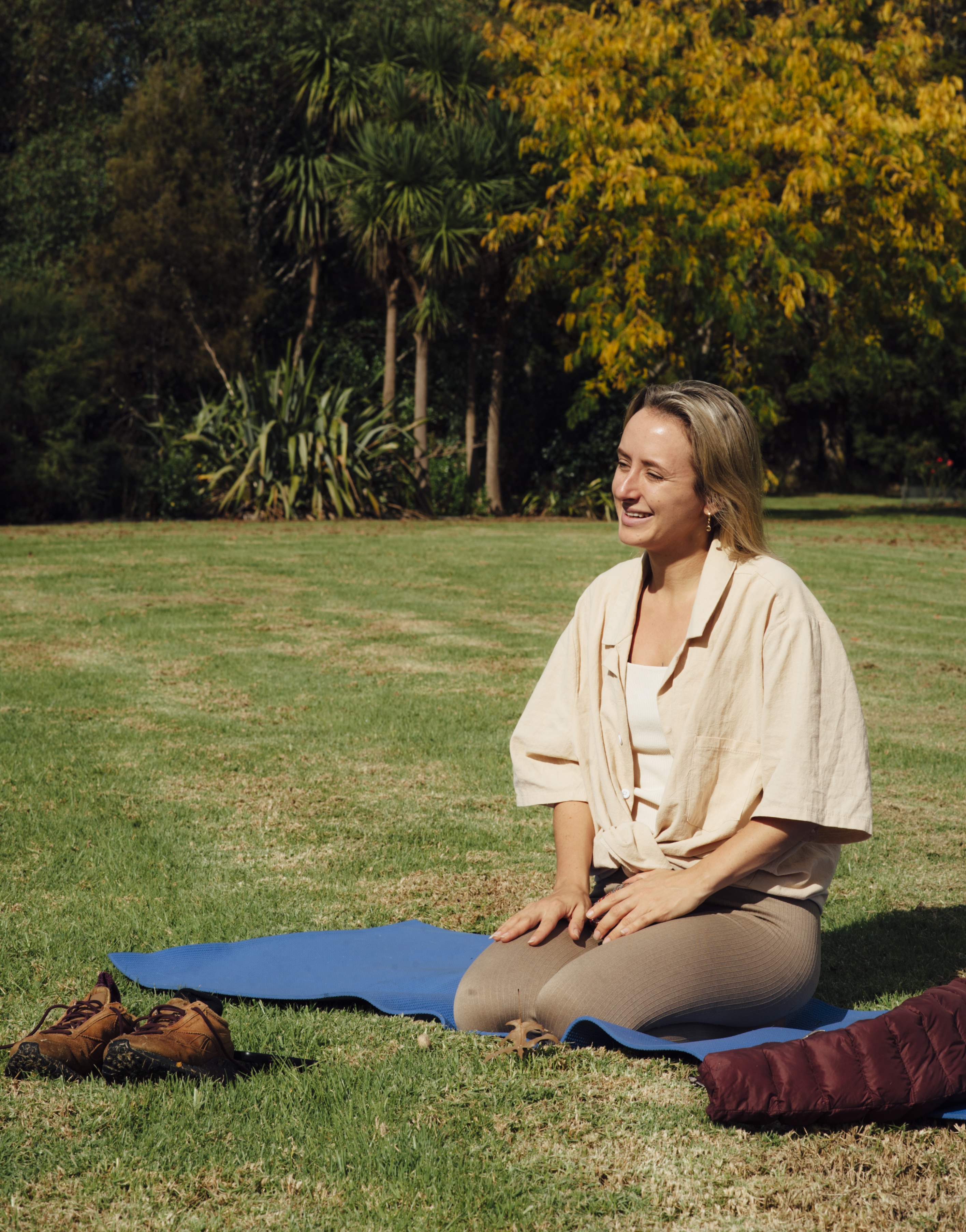 Kay sitting on a yoga mat in the park, soft afternoon light