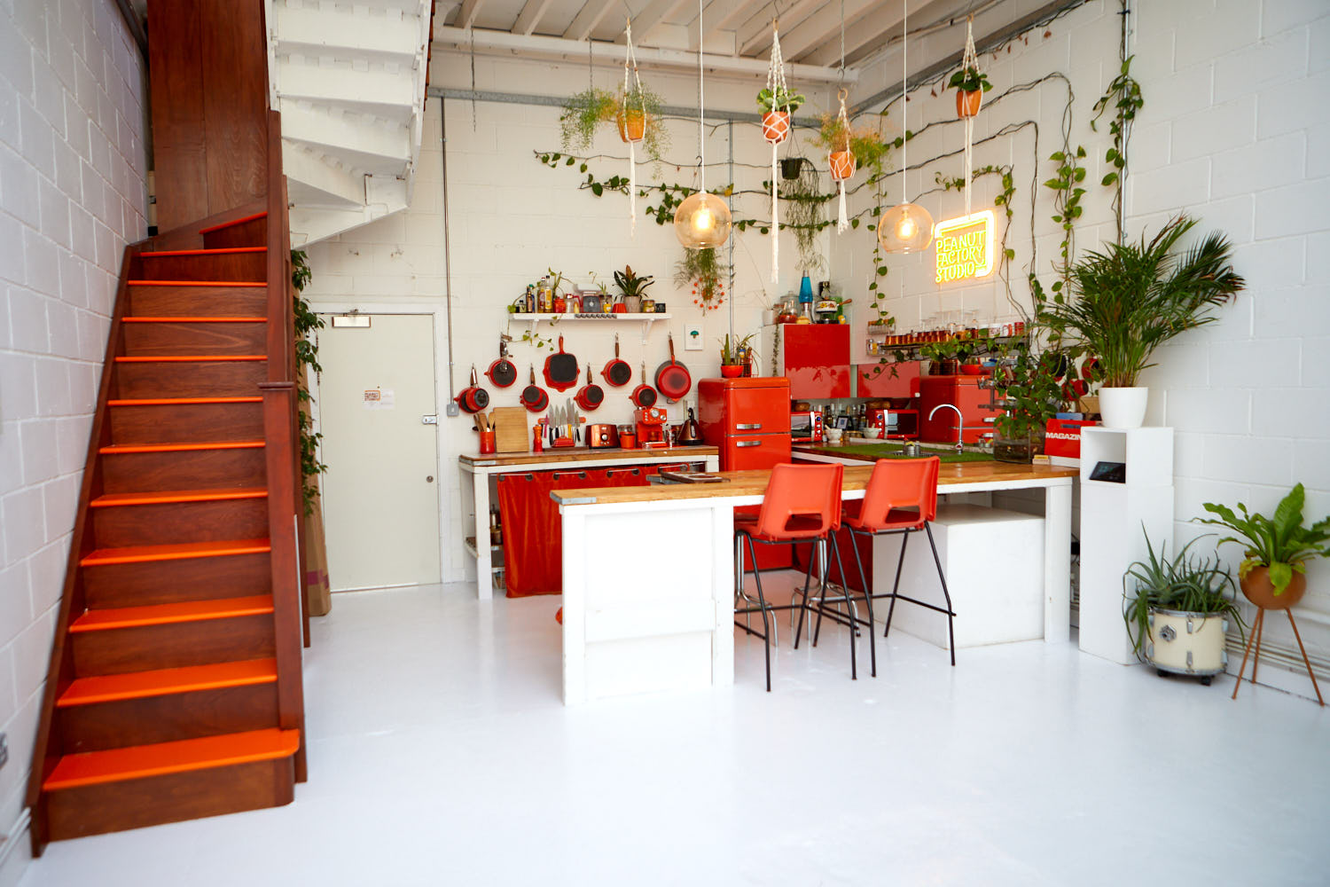 Kitchen area of the studio with red appliances, pink stairs and plants