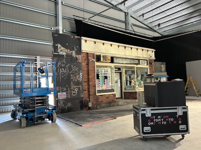 Set build inside the cover stage — brick storefront facade with scissor lift