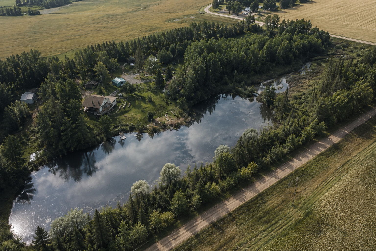 Aerial view of an Alberta acreage with a private pond surrounded by trees and farmland