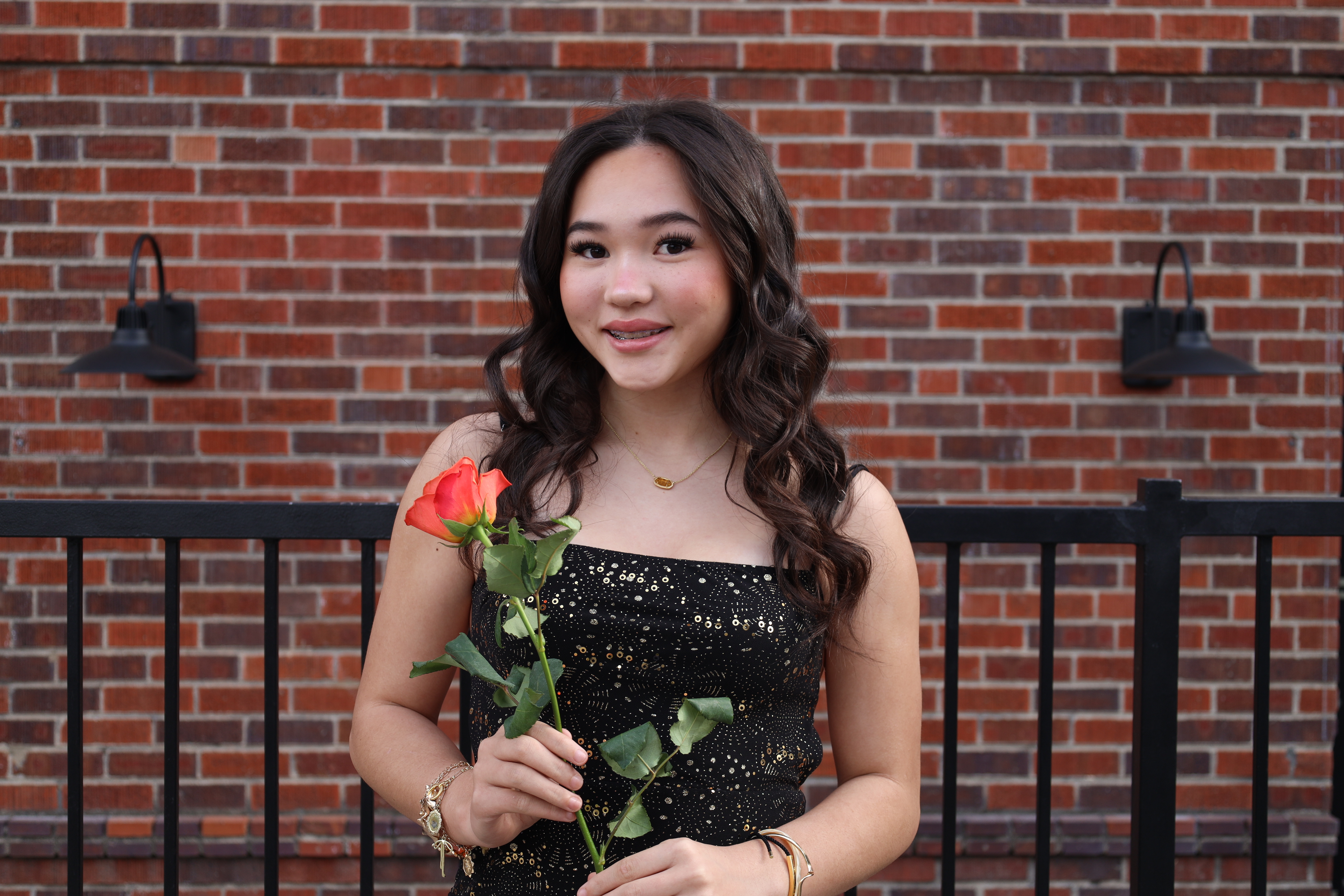 Senior in sequin dress with rose against brick