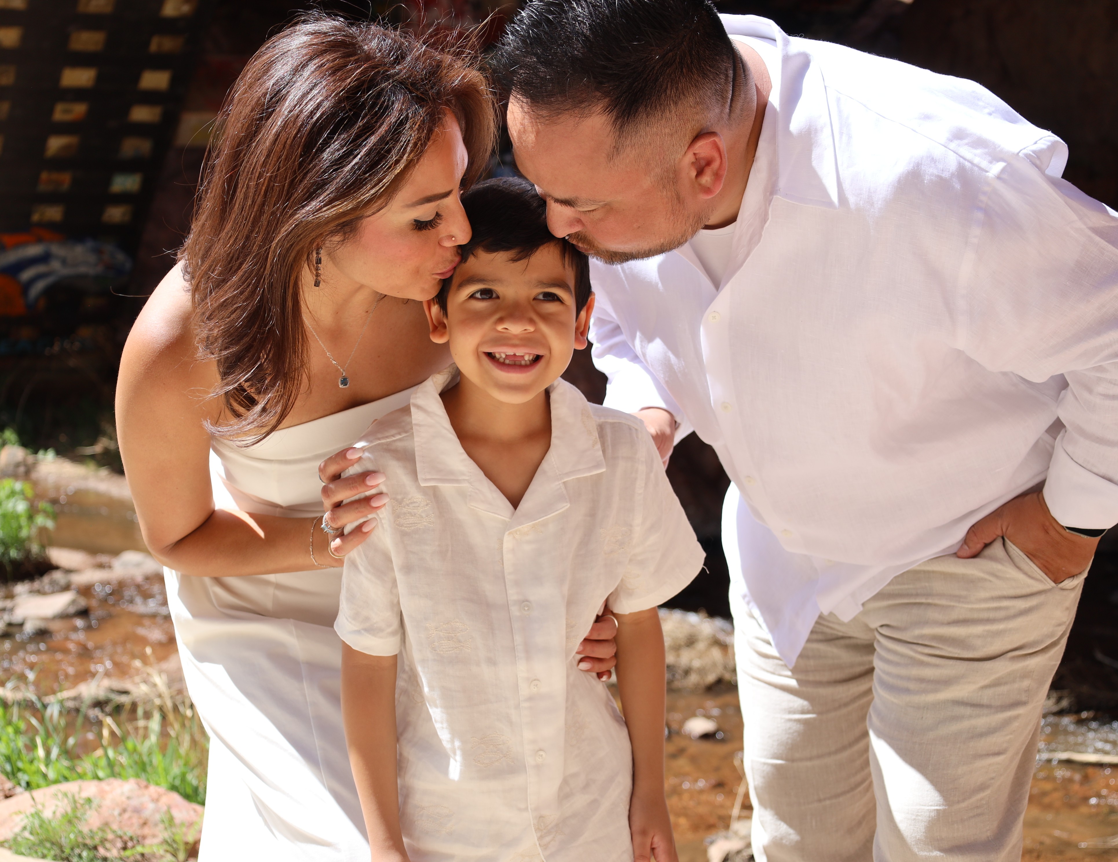Family of three in cream linens · mom kisses her son in the sun