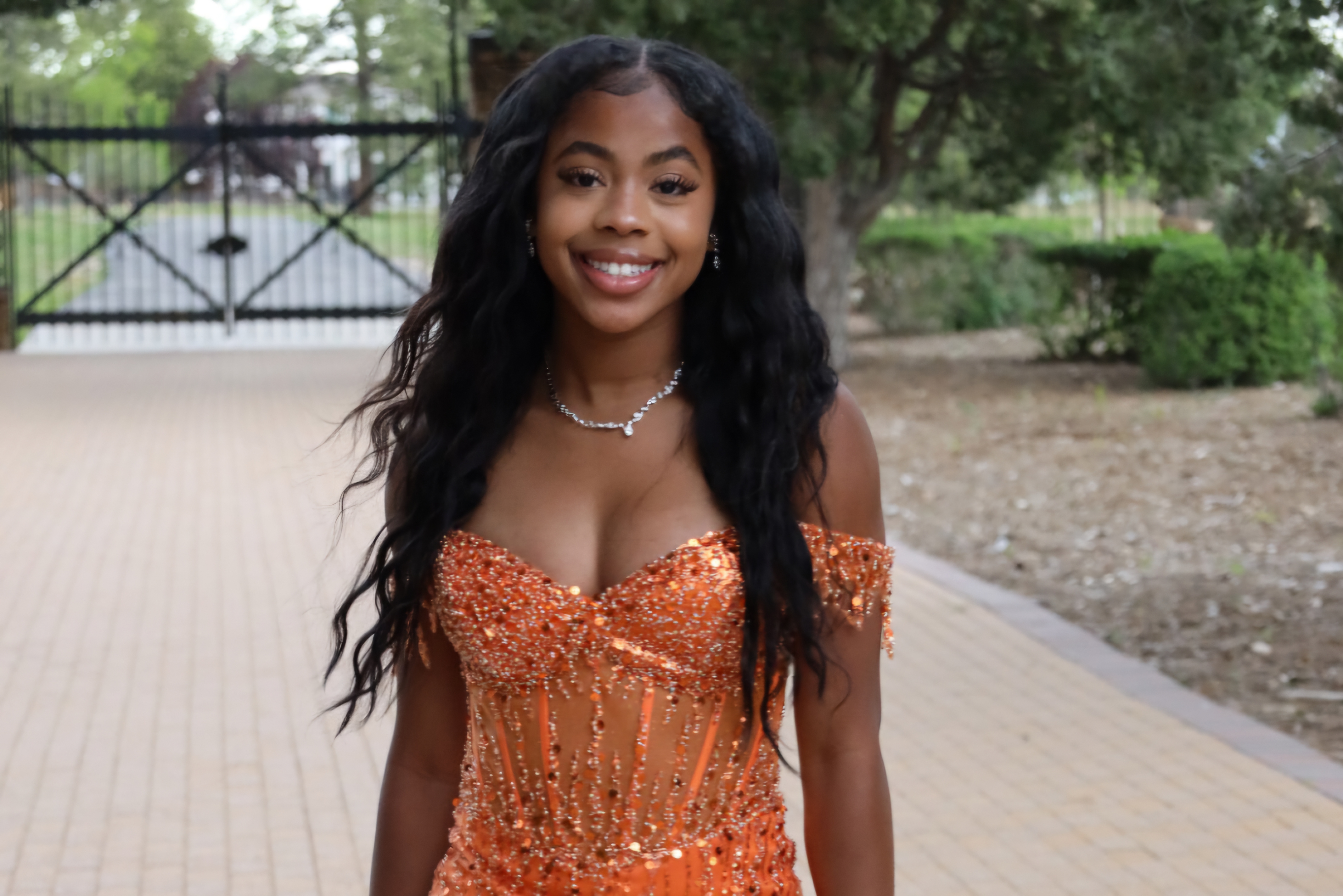 Prom portrait in orange sequin gown by the gate