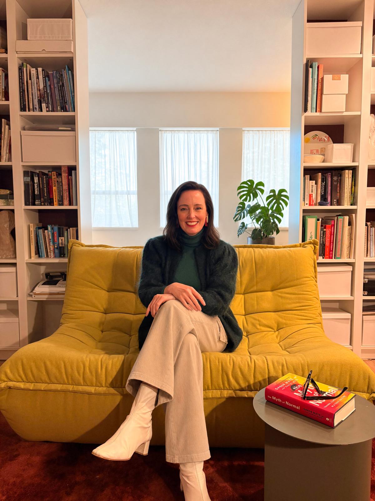 Anna, counsellor and founder of Grewp, sitting on a yellow sofa surrounded by bookshelves