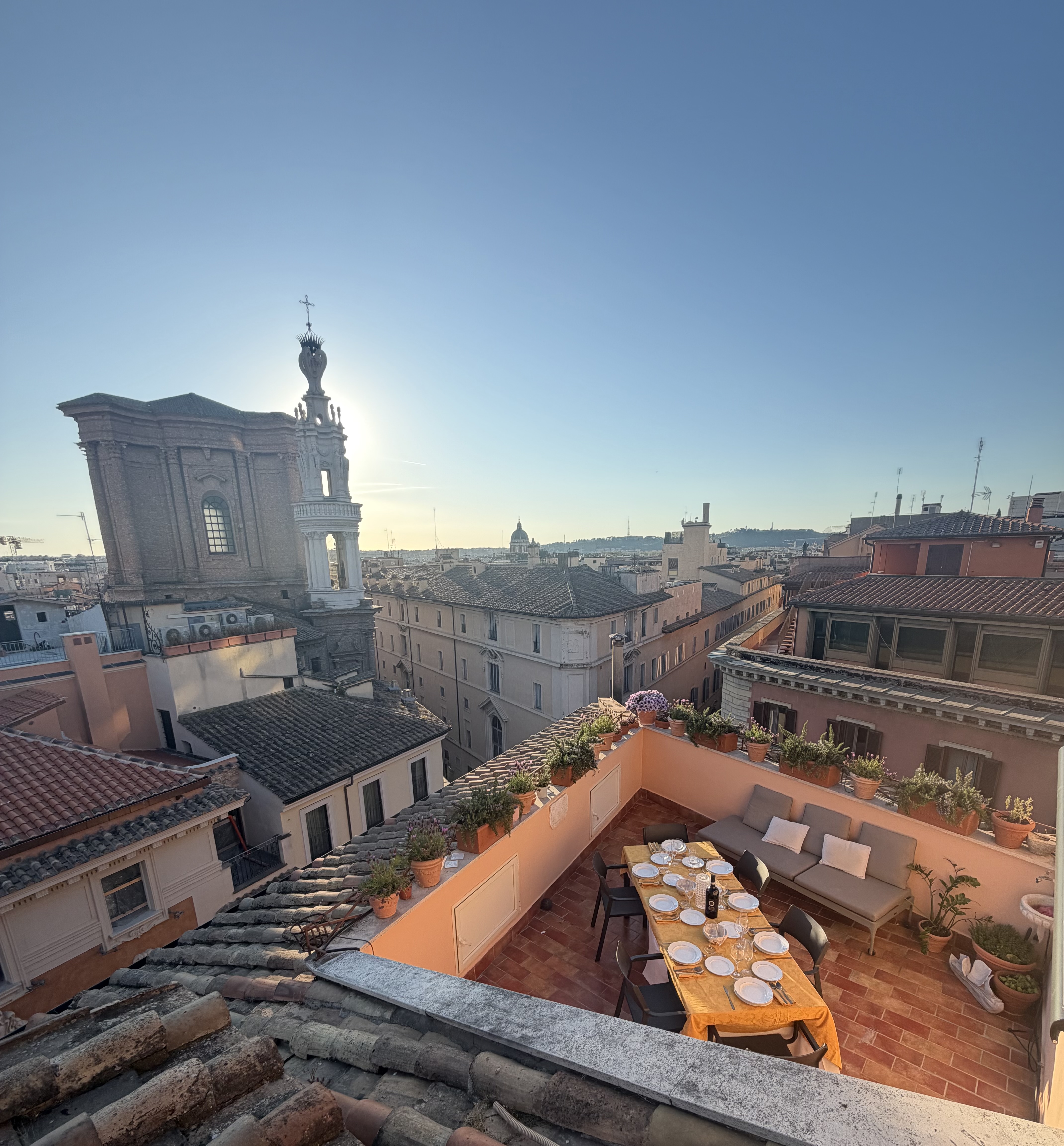 Tavolo apparecchiato sul terrazzo al tramonto con vista sui tetti di Roma
