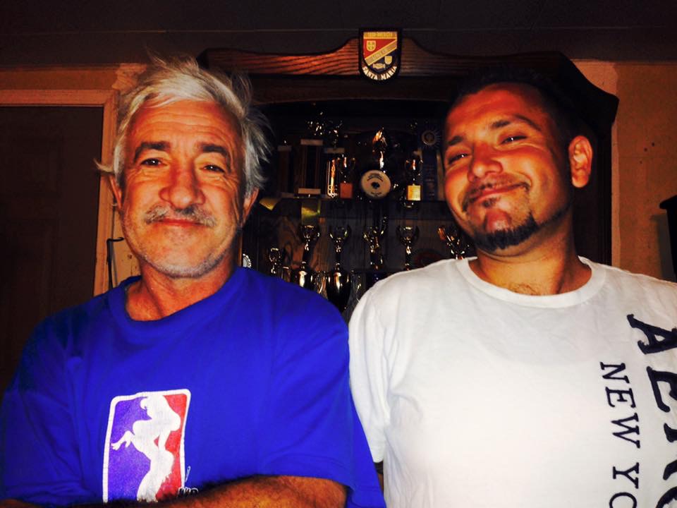 Jorge and Kevin standing together in front of a trophy case
