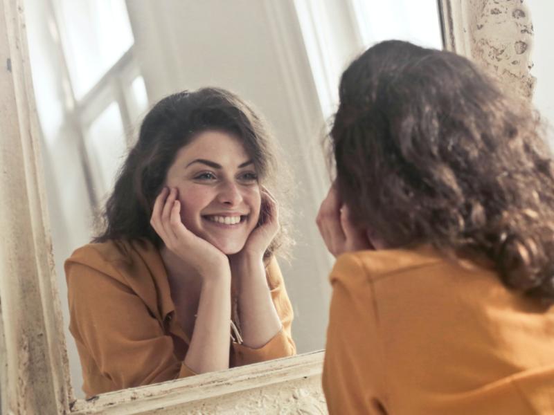 Femme souriante face à son miroir — bien-être et confiance retrouvés grâce à un accompagnement nutritionnel